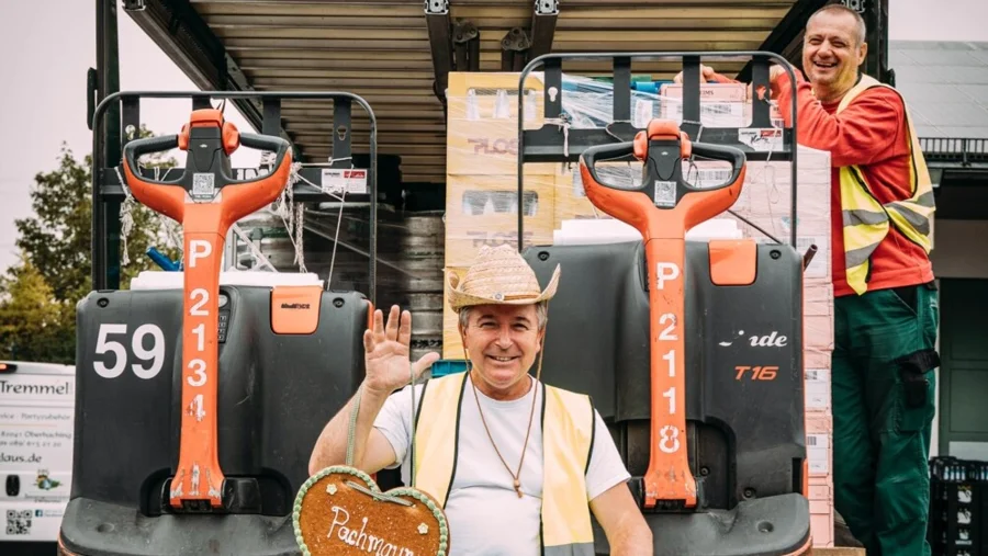 Zwei Mitarbeiter vor und auf einem Elektrohubwagen mit einem Lebkuchenherz auf dem Oktoberfest| Pachmayr im Verbund Drinkport